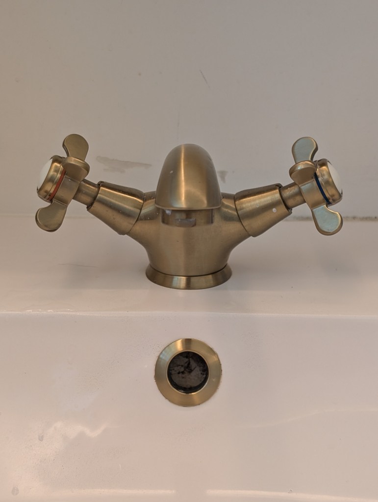 A metal faucet with two cross-shaped handles, mounted on a white sink, with a drain visible below.