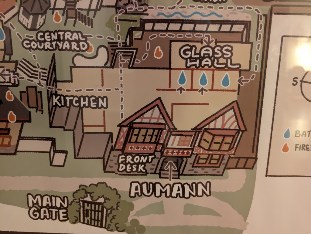 Illustrated map showing various areas of a building, including 'Central Courtyard', 'Kitchen', 'Glass Hall', 'Front Desk', and 'Aumann' labeled clearly, with a 'Main Gate' at the bottom.